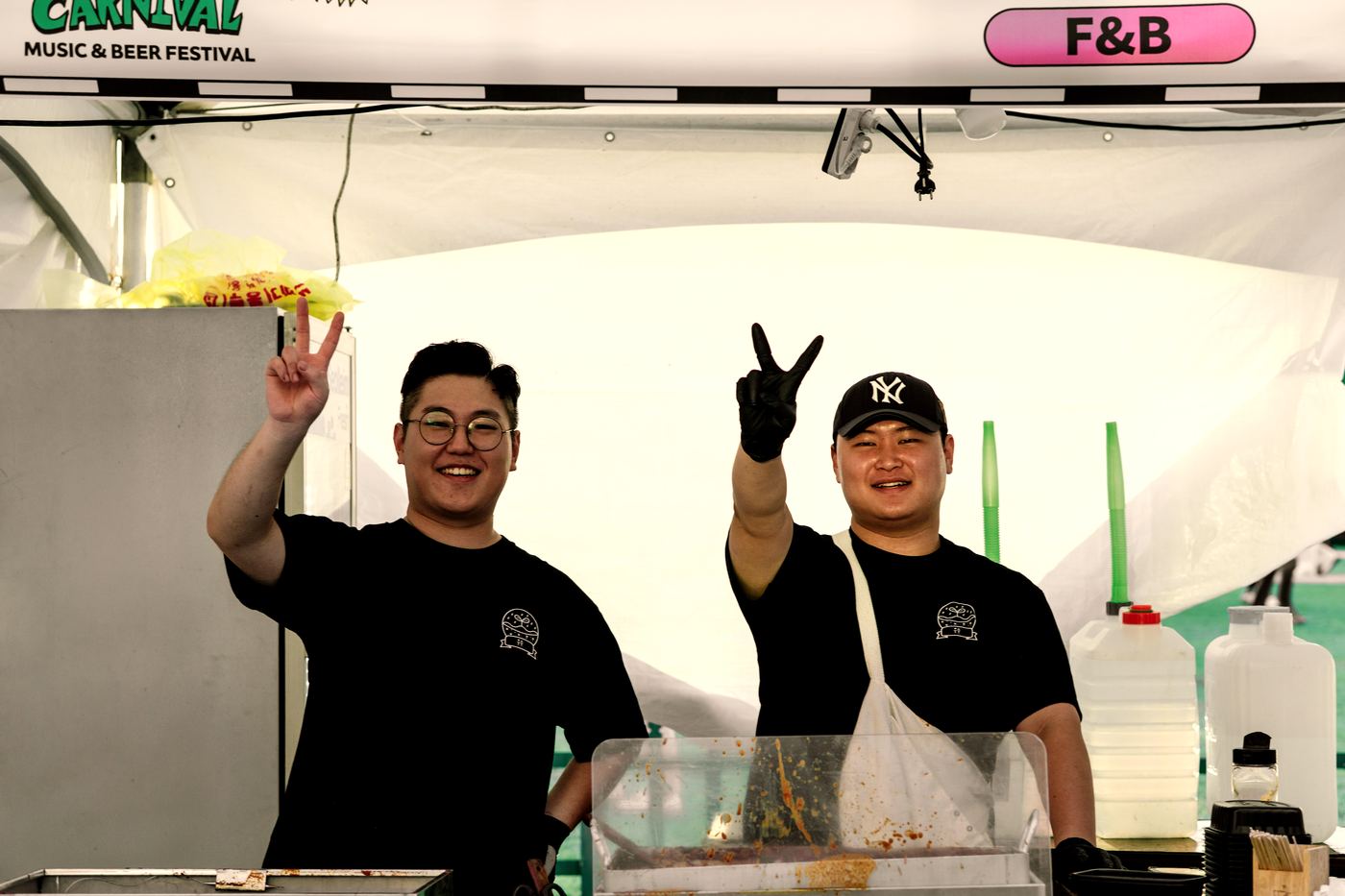 축제 부스에서 브이 사인을 하며 웃고 있는 우수분식 팀원 두 명